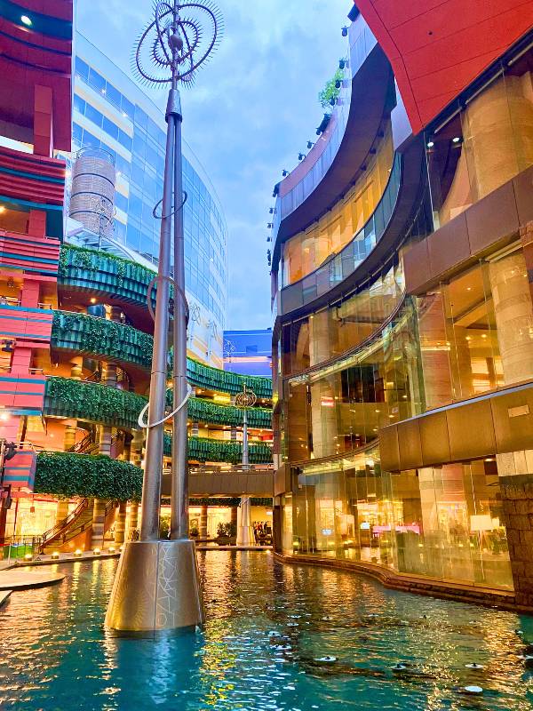 Large shopping complex with river running through it and green plants growing on the balconies.