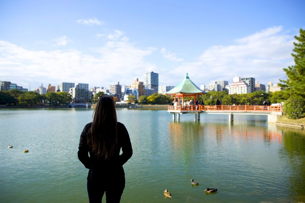 Krysti standing in front of a pond in Ohori Park with the city landscape in the background.