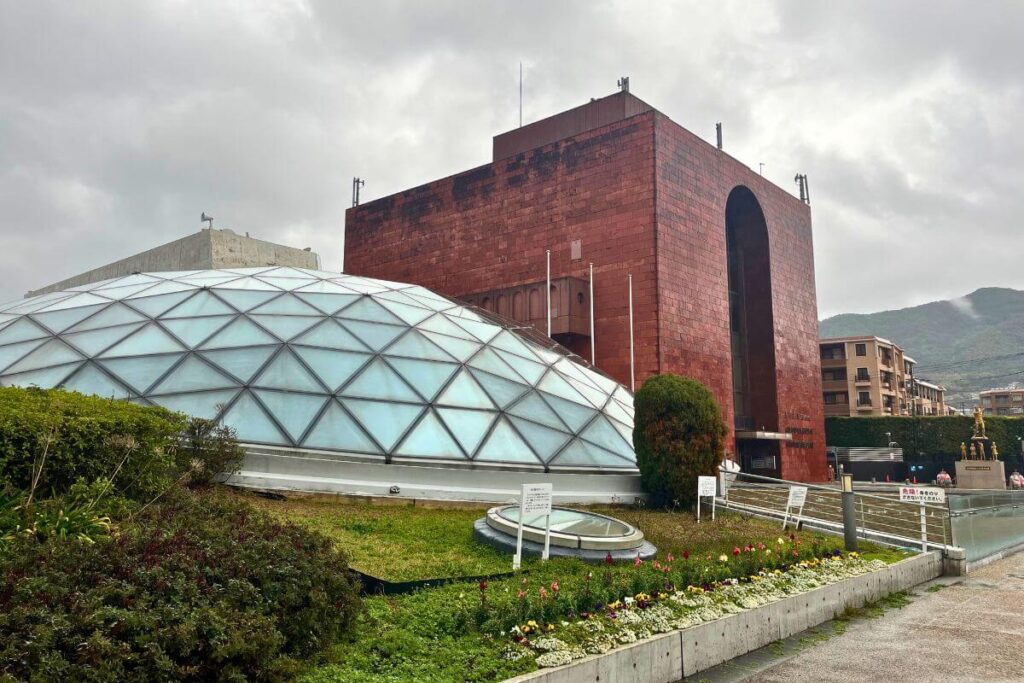 A red brick building next to a light-blue dome structure surrounded by greenery.