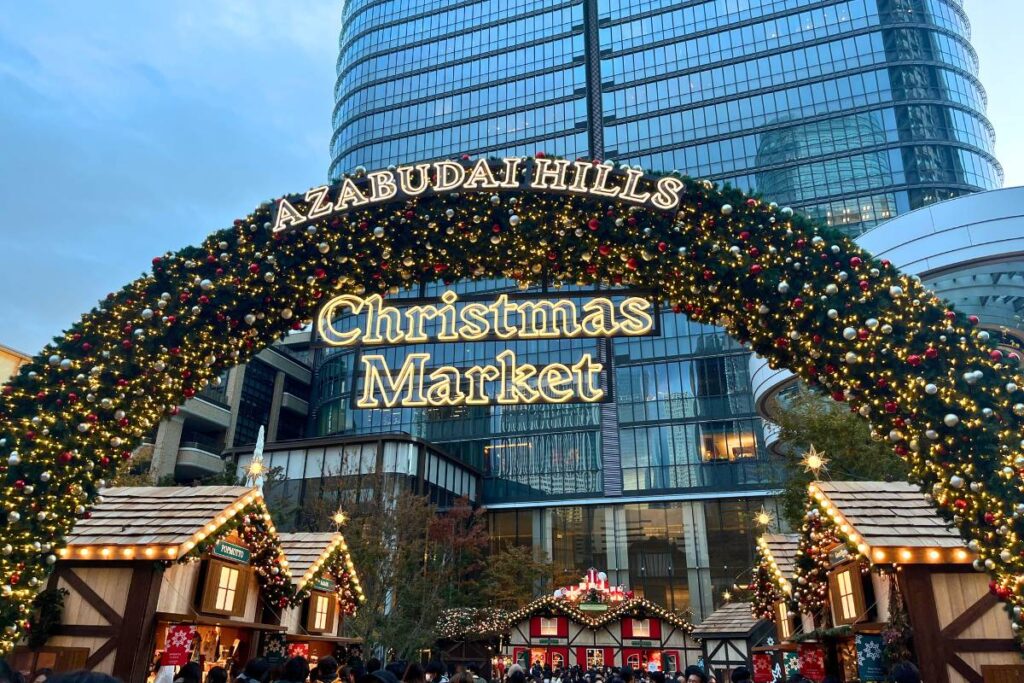 Green arch decorated with holiday ornaments and wooden stalls in the background.