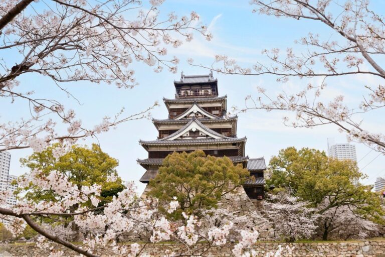 A close up of Hiroshima Castle framed by light pink flowers during cherry blossom season in Japan.