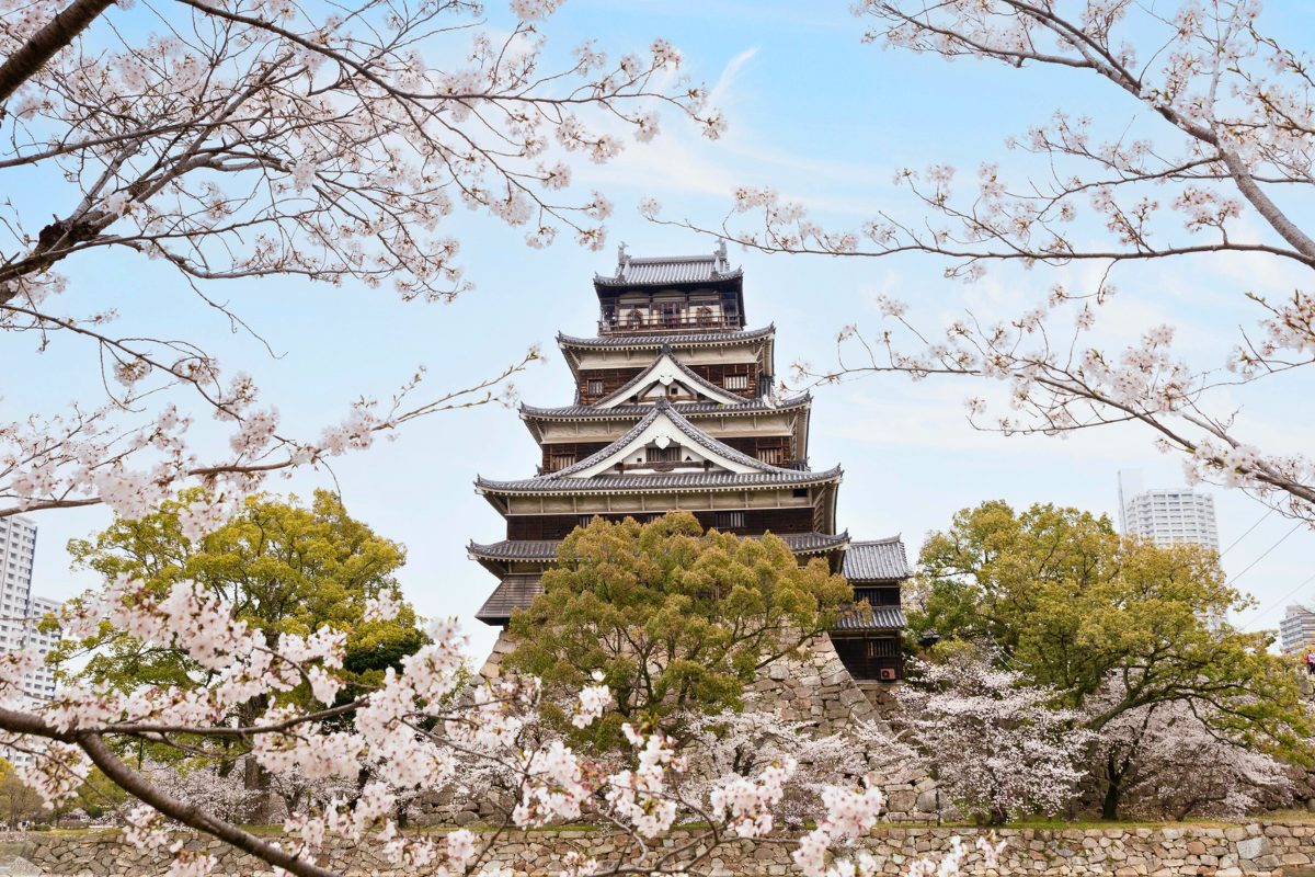A close up of Hiroshima Castle framed by light pink flowers during cherry blossom season in Japan.