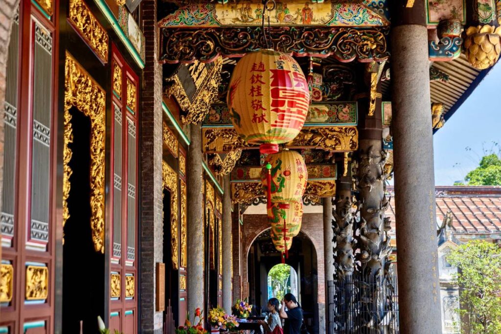 A close up of the temple's facade with intricate red and gold details and yellow lanterns.