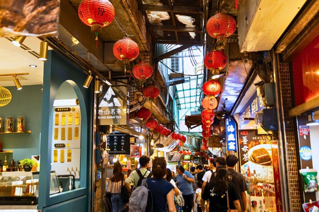 Crowded street in Jiufen - lined with shops, food stalls, and red lanterns.