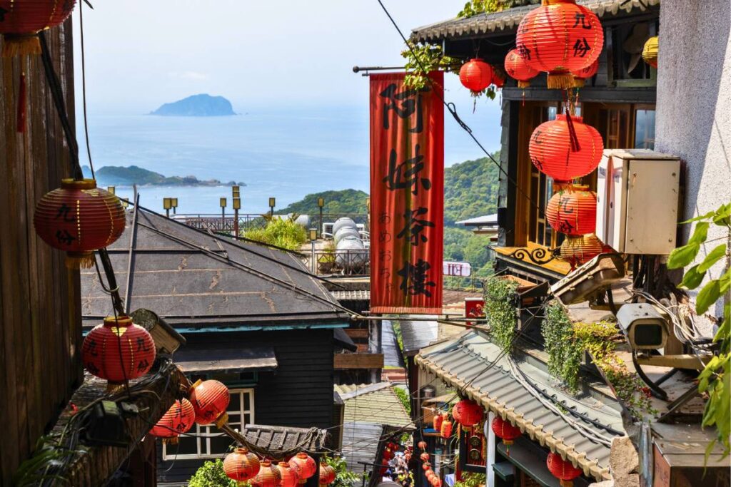 Red lanterns line a small pathway with views of the ocean in the distance.