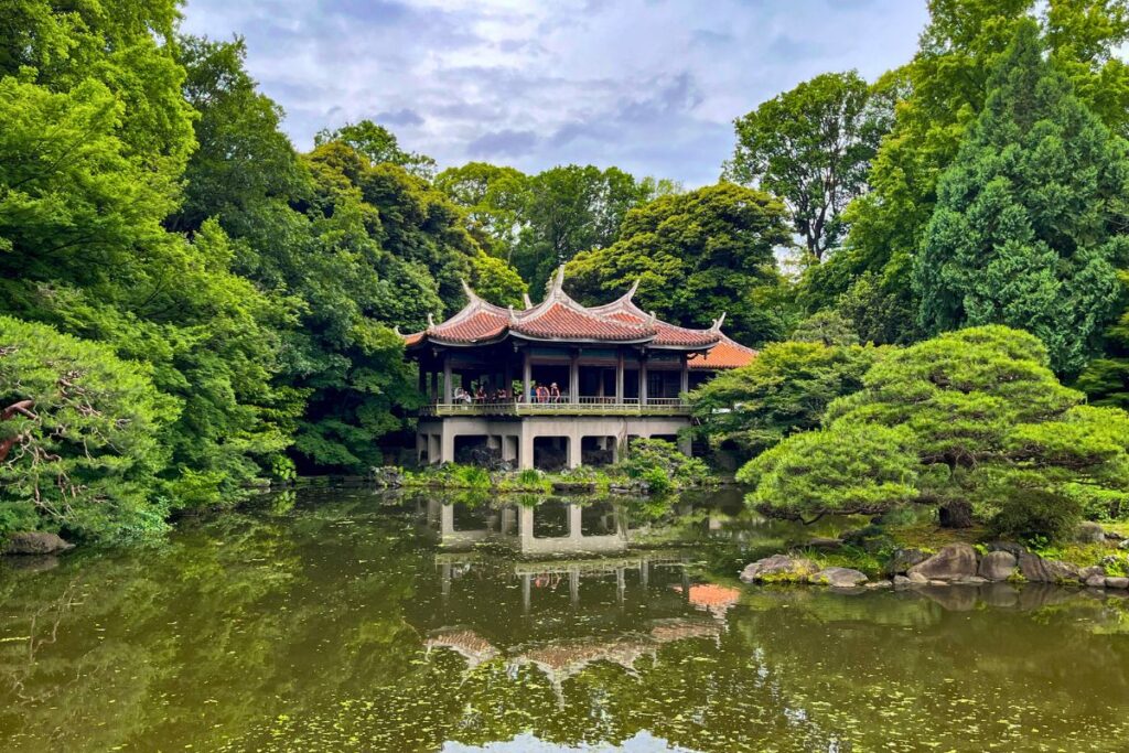 A pagoda in Gyoen National Park reflected in a pond and surrounded by lush greenery.