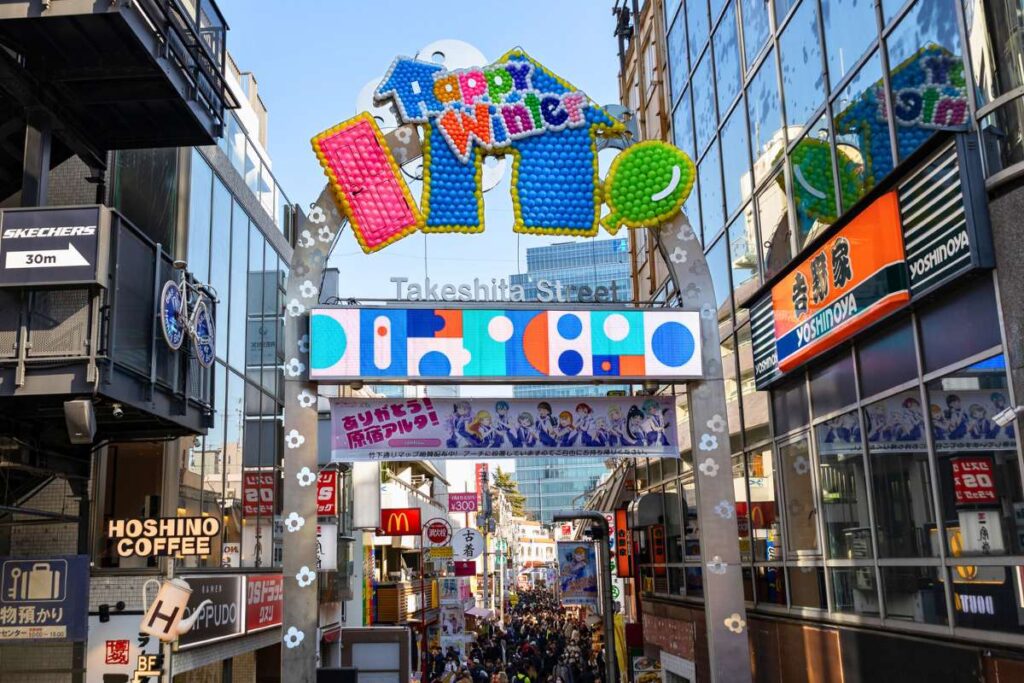 Bright archway marking the start of Takeshita Street with crowds of people behind it.