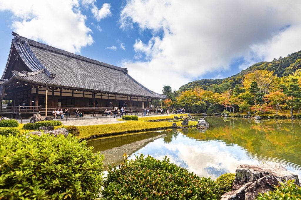 A pond set in front of a traditional Zen temple surrounded by fall foliage.