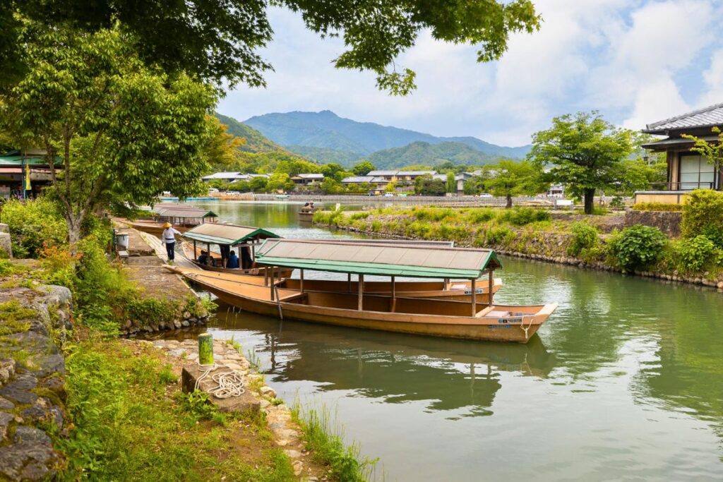 A traditional Japanese boat docked in the river surrounded by green trees with mountains in the background.