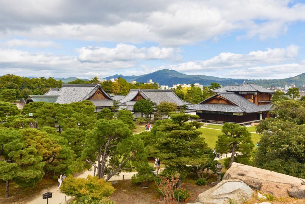 View overlooking Nijo Castle surrounding by green trees with mountains in the background.