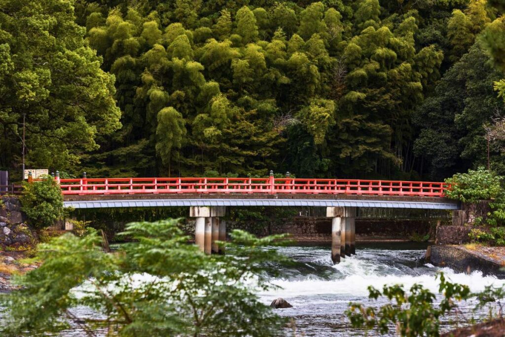 Red bridge surrounded by lush green trees with rushing water below.