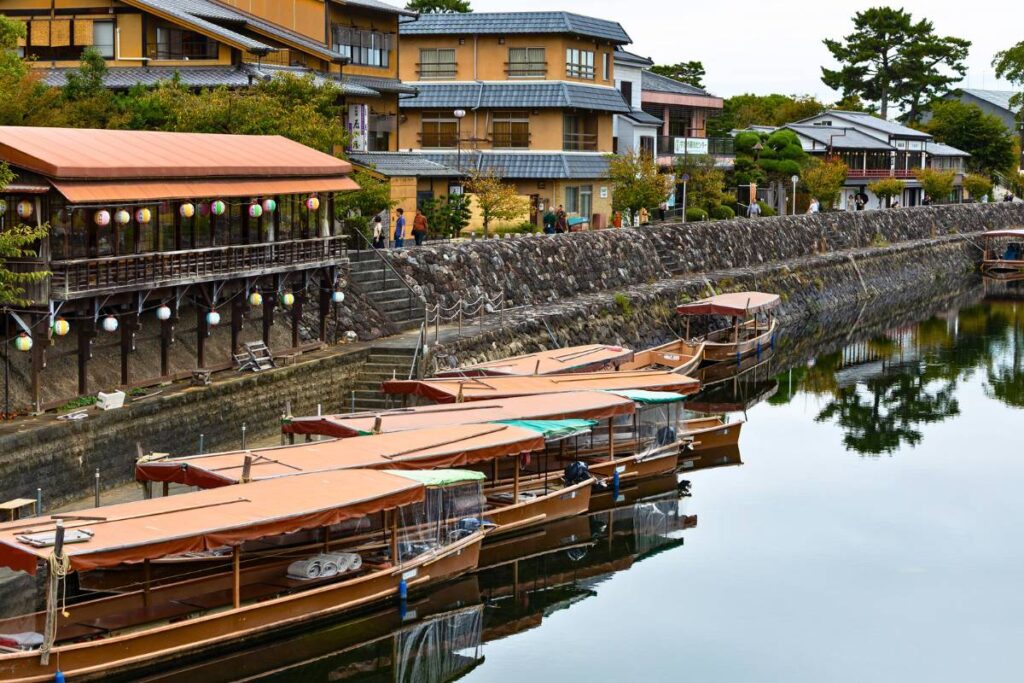 Boats docked along the Uji River with Japanese houses and businesses in the background.
