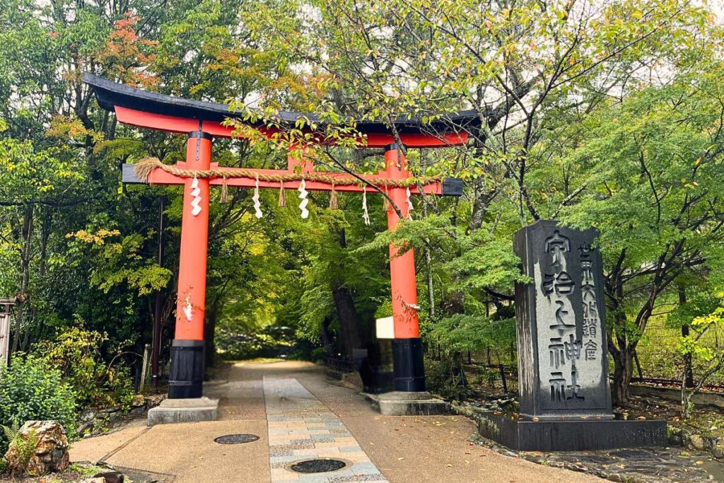 A red torii gate marking the entrance to a path that leads through the forest.