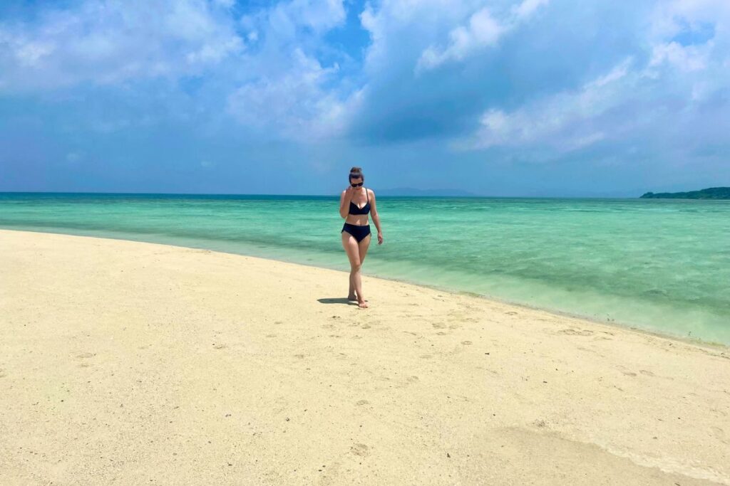 Krysti walking along the beach with blue-green waters in the background.