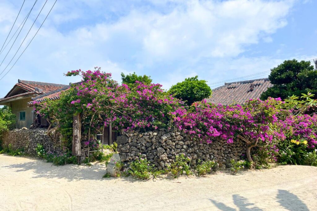 A traditional home on Taketomi Island with a red-tiled roof surrounding by a stone wall and bright pink flowers.