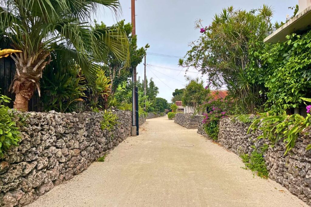 An empty sandy street in Taketomi lined with stone walls.