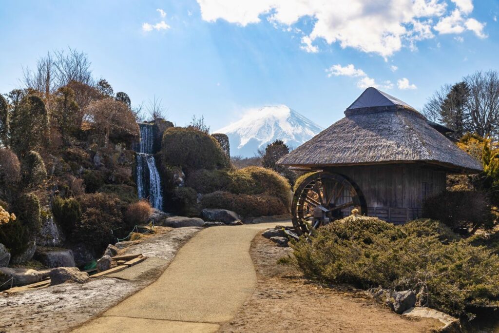 Mount Fuji framed behind a small village with a thatched-roof house.