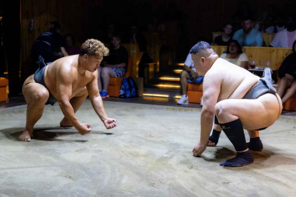 Two sumo wrestlers crouching down in preparation to begin a match at the Asakusa Sumo Club.