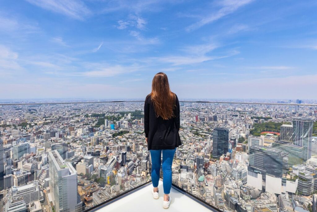 Krysti standing at the corner of Shibuya Sky's rooftop facing the city skyline.
